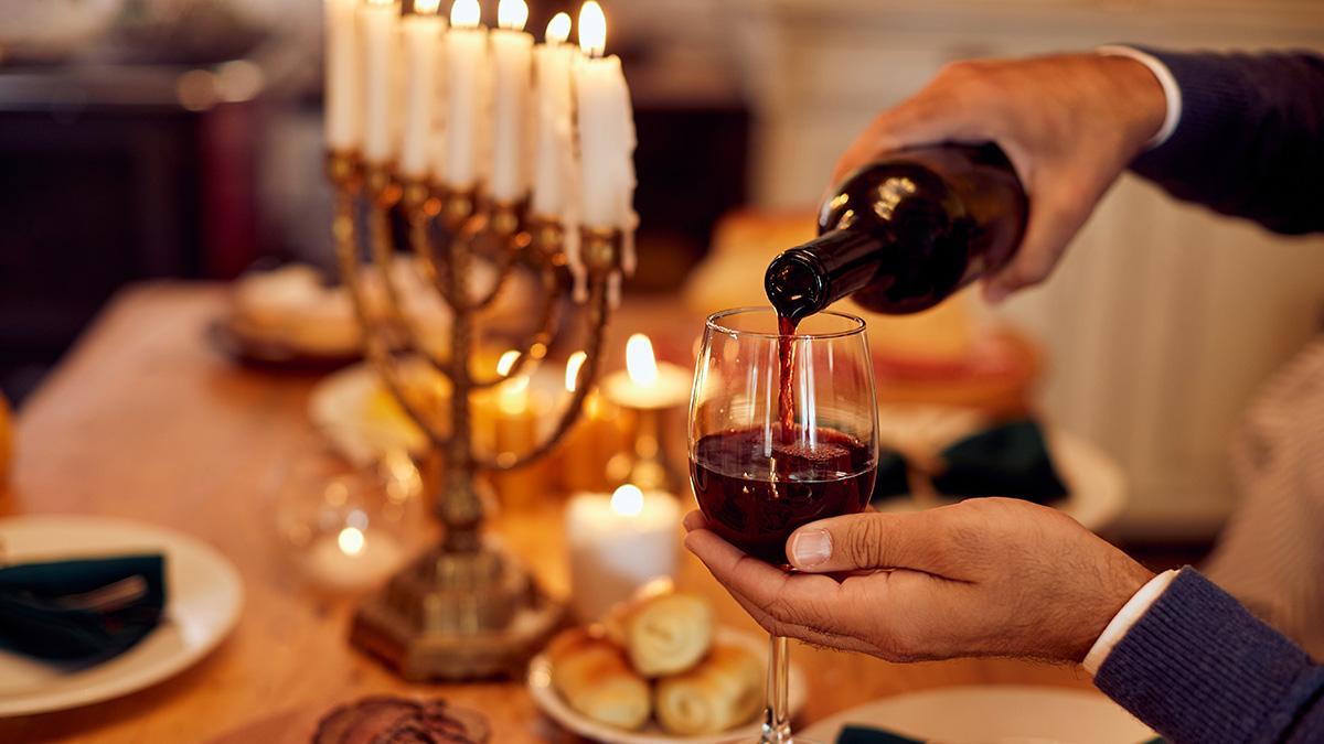 Article Cards Featured Image Close up of Jewish man pours wine while having meal at dining table on Hanukkah.