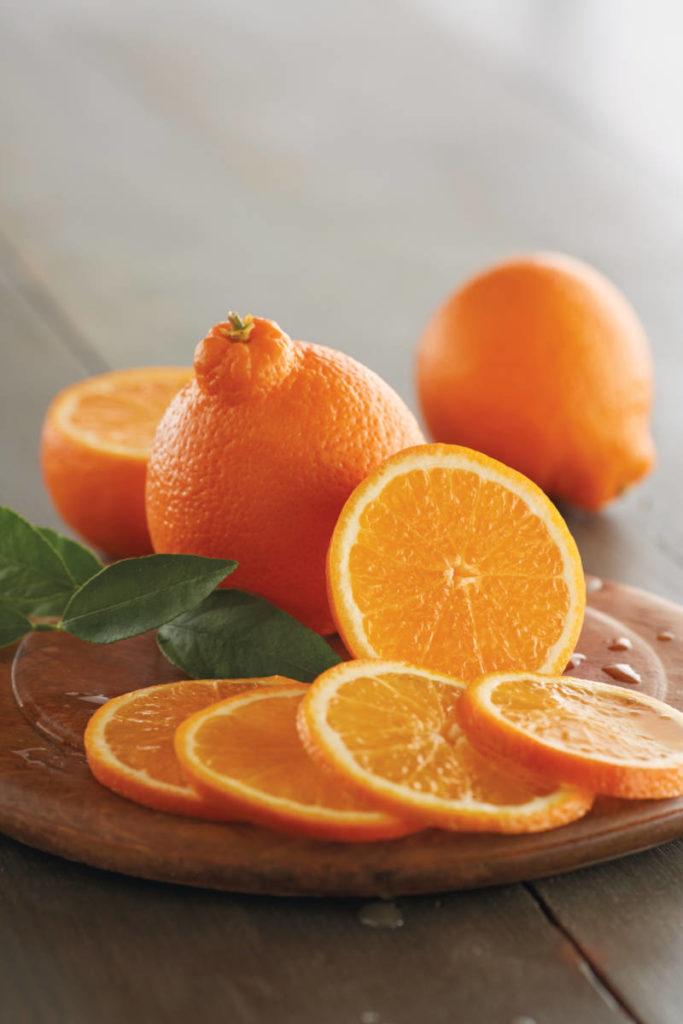 A photo of honeybell oranges on a wooden plate, some whole and some sliced.