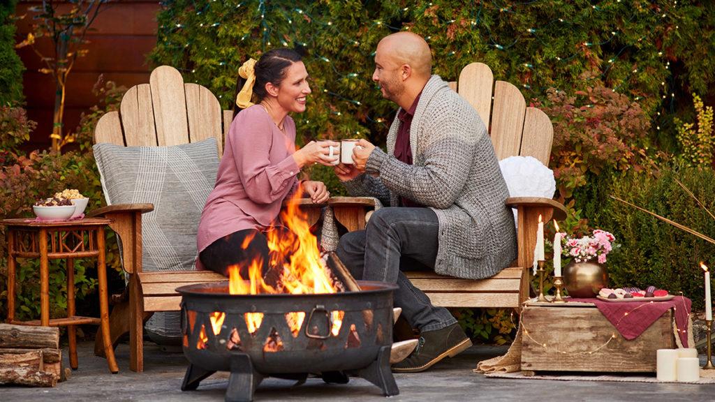 A photo of a winter wonderland with a couple sipping coco while sitting next to an outdoor fire pit