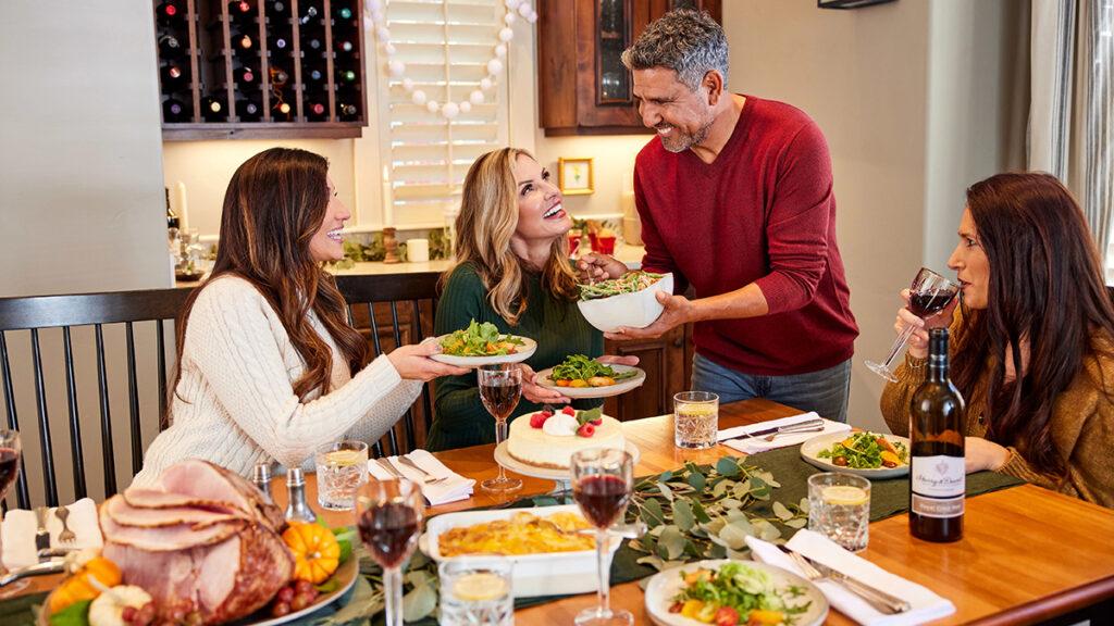 Dinner guest etiquette with a man serving food to three women sitting at a table.