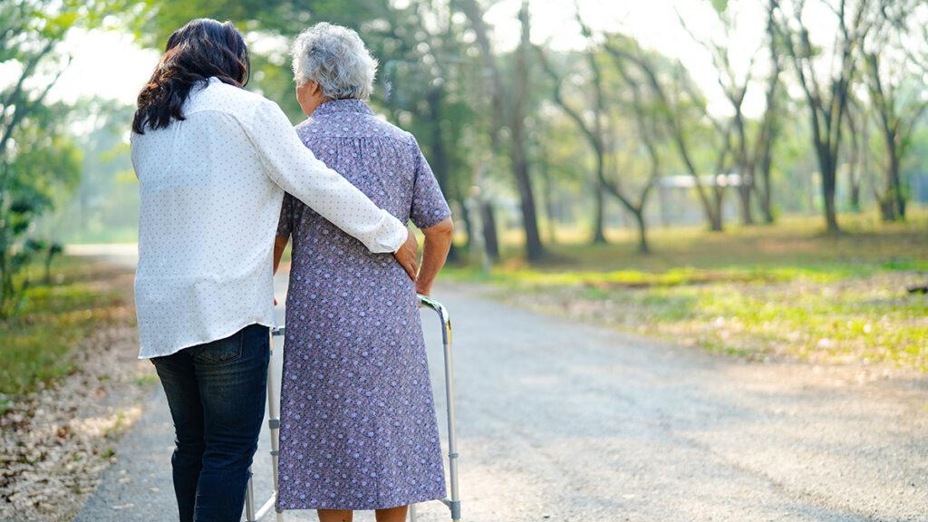 Caregiver walking with another woman using a walker outside.