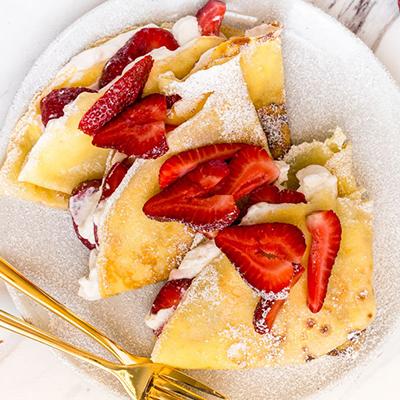 Breakfast for dinner with a plate of crêpes topped with strawberries.